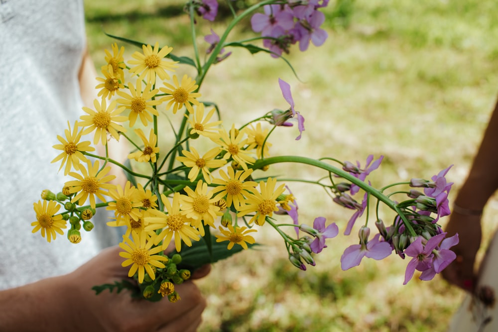 a person holding a bouquet of yellow and purple flowers