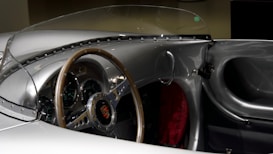 A classic car interior featuring a sleek vintage dashboard with multiple gauges and a wooden steering wheel, encapsulated by a minimalist design and a small windshield.