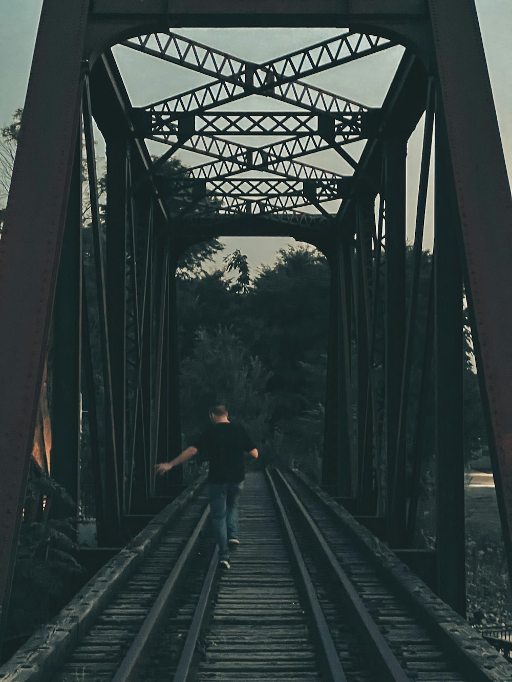 a man walking across a train track under a bridge
