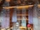 An elegant interior featuring a stunning ceiling installation with hanging crystal-like decorations creating a shimmering effect. Large reflective orbs in silver and red are suspended, enhancing the luxurious ambiance. The lighting is warm, with decorative lights embedded in the ceiling.