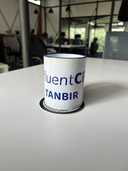 Entrepreneur holding a black and gold mug, smiling confidently in a sunlit office with modern decor.