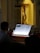 A person is playing or reading sheet music from a music stand with a religious statue of Jesus on the cross in the background, inside a dimly lit church.