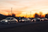 A group of smiling drivers enjoying a warm sunset beside vintage cars.