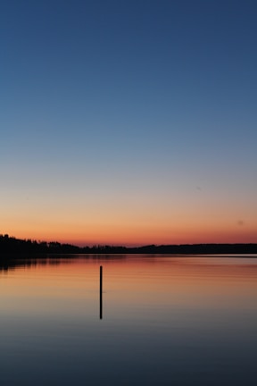 A serene outdoor shot of a solo founder reflecting by a quiet lake at sunset.