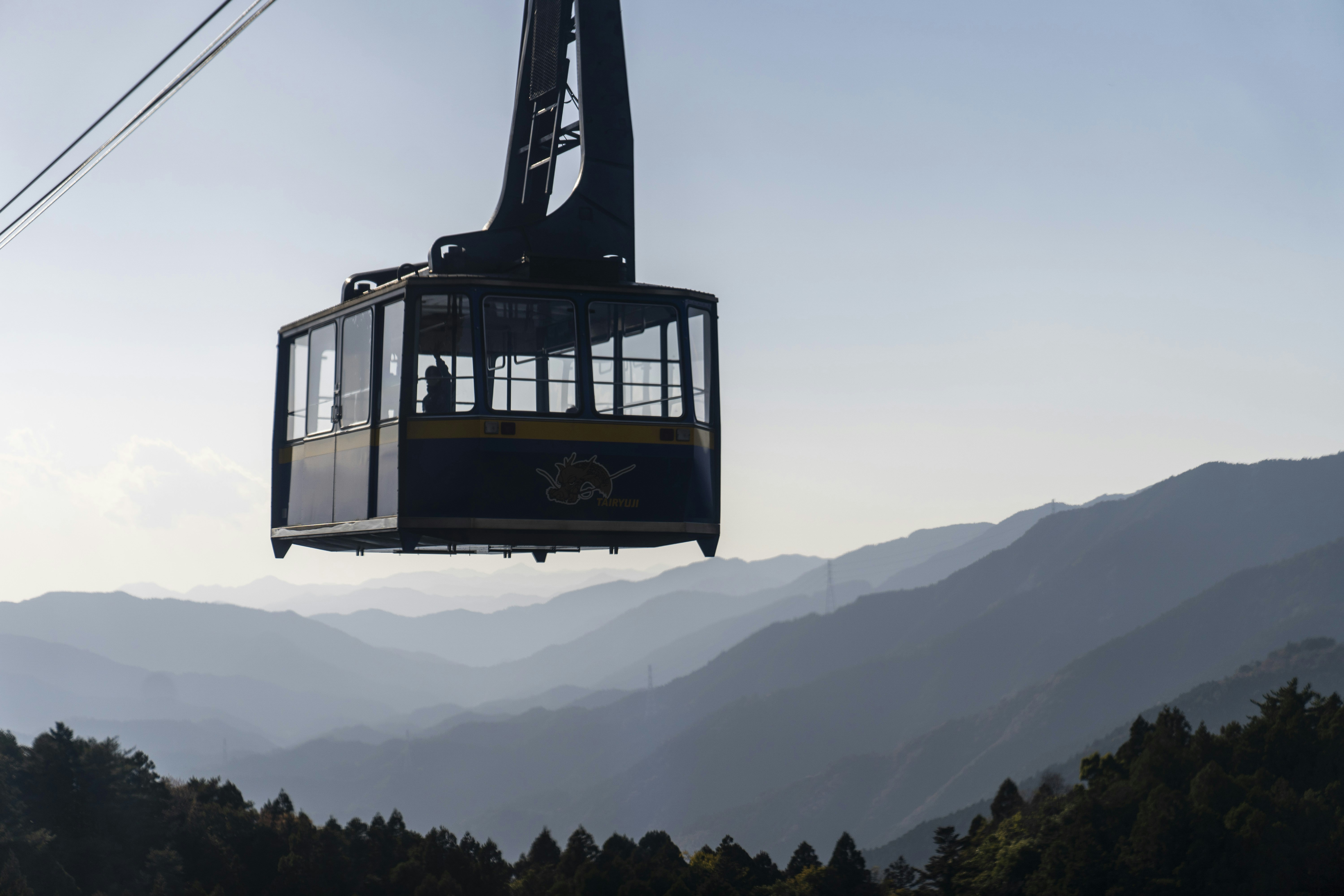 a cable car going up a mountain with mountains in the background, Taking the Ropeway to Temple 21.