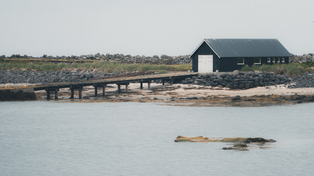 a black house sitting on top of a beach next to a body of water