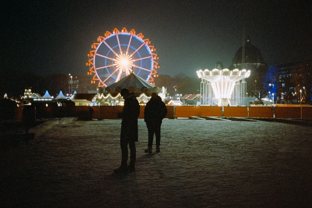 two people standing in front of a ferris wheel at night