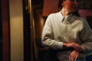 A relaxed, sophisticated man wearing a tailored sweater in a neutral-toned modern interior with soft shadows.