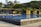 A modern swimming pool with clear blue water, surrounded by a contemporary structure adorned with greenery. Trees and overhanging plants add a natural feel to the sleek architectural design.