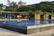 A modern swimming pool with clear blue water, surrounded by a contemporary structure adorned with greenery. Trees and overhanging plants add a natural feel to the sleek architectural design.