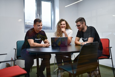 a group of people sitting around a table with laptops