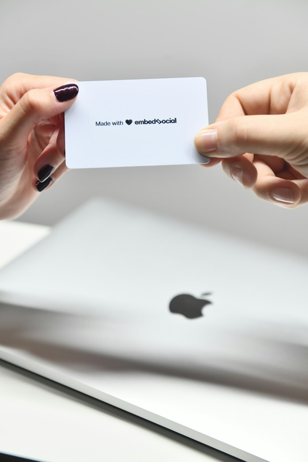 two hands holding a business card over a laptop