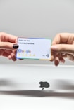 two hands holding a google credit card in front of an apple logo