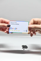 two hands holding a google credit card in front of an apple logo