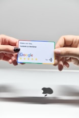 two hands holding a google credit card in front of an apple logo