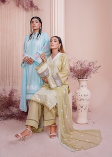 Two elegant women in soft white and beige tones, surrounded by delicate gold accents, symbolizing calm and radiant beauty.