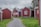 Several small, red wooden cottages with white trim situated along a gravel pathway, surrounded by green grass and trees on a cloudy day.