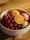 Close-up of a bright, hand-crafted ceramic bowl filled with fresh fruit on a rustic table.