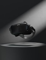 A virtual reality headset floating above a circular platform is illuminated by a spotlight. The surrounding area is dark, highlighting the sleek design of the device.