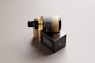 A sleek, amber glass bottle with a dropper cap is resting on its side on top of a rectangular black box. The packaging features minimalist design elements with gold and white text, conveying a sense of luxury and sophistication. The background is a neutral tone, highlighting the elegant design of the bottle and box.