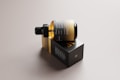 A sleek, amber glass bottle with a dropper cap is resting on its side on top of a rectangular black box. The packaging features minimalist design elements with gold and white text, conveying a sense of luxury and sophistication. The background is a neutral tone, highlighting the elegant design of the bottle and box.