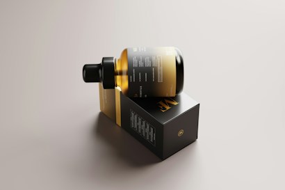 A sleek, amber glass bottle with a dropper cap is resting on its side on top of a rectangular black box. The packaging features minimalist design elements with gold and white text, conveying a sense of luxury and sophistication. The background is a neutral tone, highlighting the elegant design of the bottle and box.