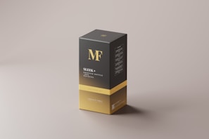 A sleek rectangular box with a minimalist design, primarily in black and gold. The box features bold typography with the initials 'MF' at the top and the text 'Sleek + Dropper Bottle Box Mockups' below. The design is clean and modern, with a soft shadow cast on the neutral background.
