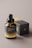 A dark-colored dropper bottle with the label 'SLEEK+ DROP BOTTLE MOCKUPS' is positioned in front of a matching box. The bottle features a gradient from black to gold, complemented by a shiny black dropper cap. The box is predominantly black with gold lettering and detailing.