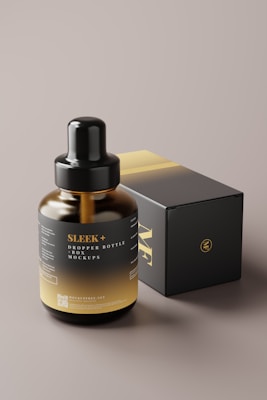 A dark-colored dropper bottle with the label 'SLEEK+ DROP BOTTLE MOCKUPS' is positioned in front of a matching box. The bottle features a gradient from black to gold, complemented by a shiny black dropper cap. The box is predominantly black with gold lettering and detailing.