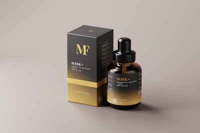 A droplet bottle with a black dropper cap stands beside a black and gold packaging box. The box and the bottle both have the words 'SLEEK + DROPPER BOTTLE MOCKUPS' printed on them in gold lettering, along with the letters 'MF' prominently displayed on the box. The overall design is elegant and minimalist, featuring a smooth matte finish.