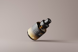 A sleek, modern bottle with a black and gold label is floating against a neutral background. The bottle has a minimalist design with clean lines and a matte finish. The label includes text and a QR code, indicating it likely contains a product for personal care or wellness.