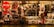 A brightly lit shop window displays a variety of Christmas-themed decorations, including nutcrackers, Santa figures, wreaths, and stockings. The display is richly colored with reds and greens, enhanced by warm lighting. A person stands inside, arranging items on the shelves.
