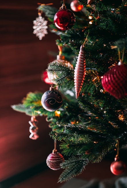 A decorated Christmas tree with various ornaments including red and pink baubles, snowflakes, and spiral-shaped decorations. The tree is adorned with lights, creating a warm and festive atmosphere.
