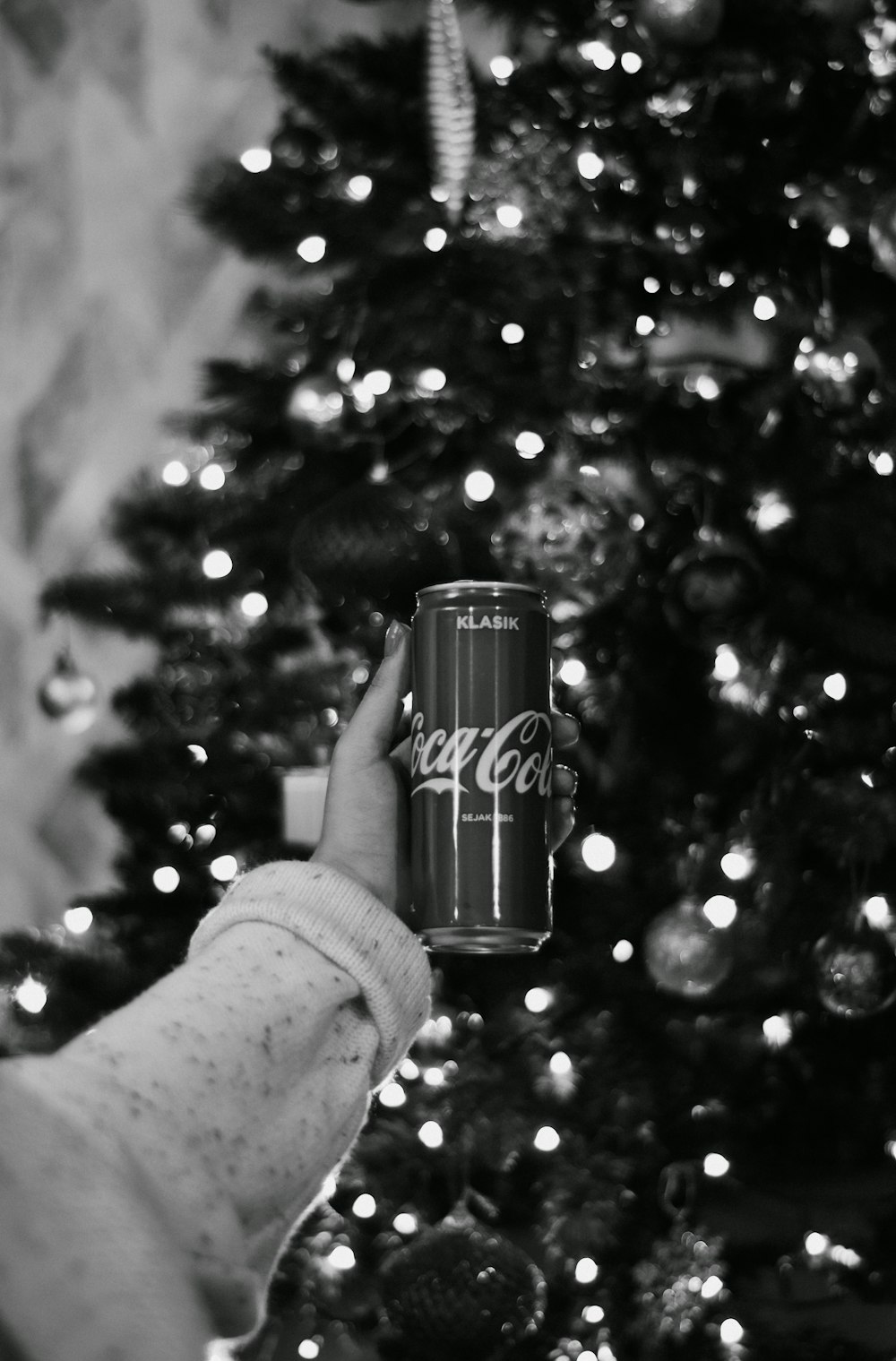 a woman holding a can of coca cola in front of a christmas tree