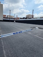 A flat rooftop area with a level tool placed on the surface. The sky above is partly cloudy with several pipes and ventilation systems visible in the background.