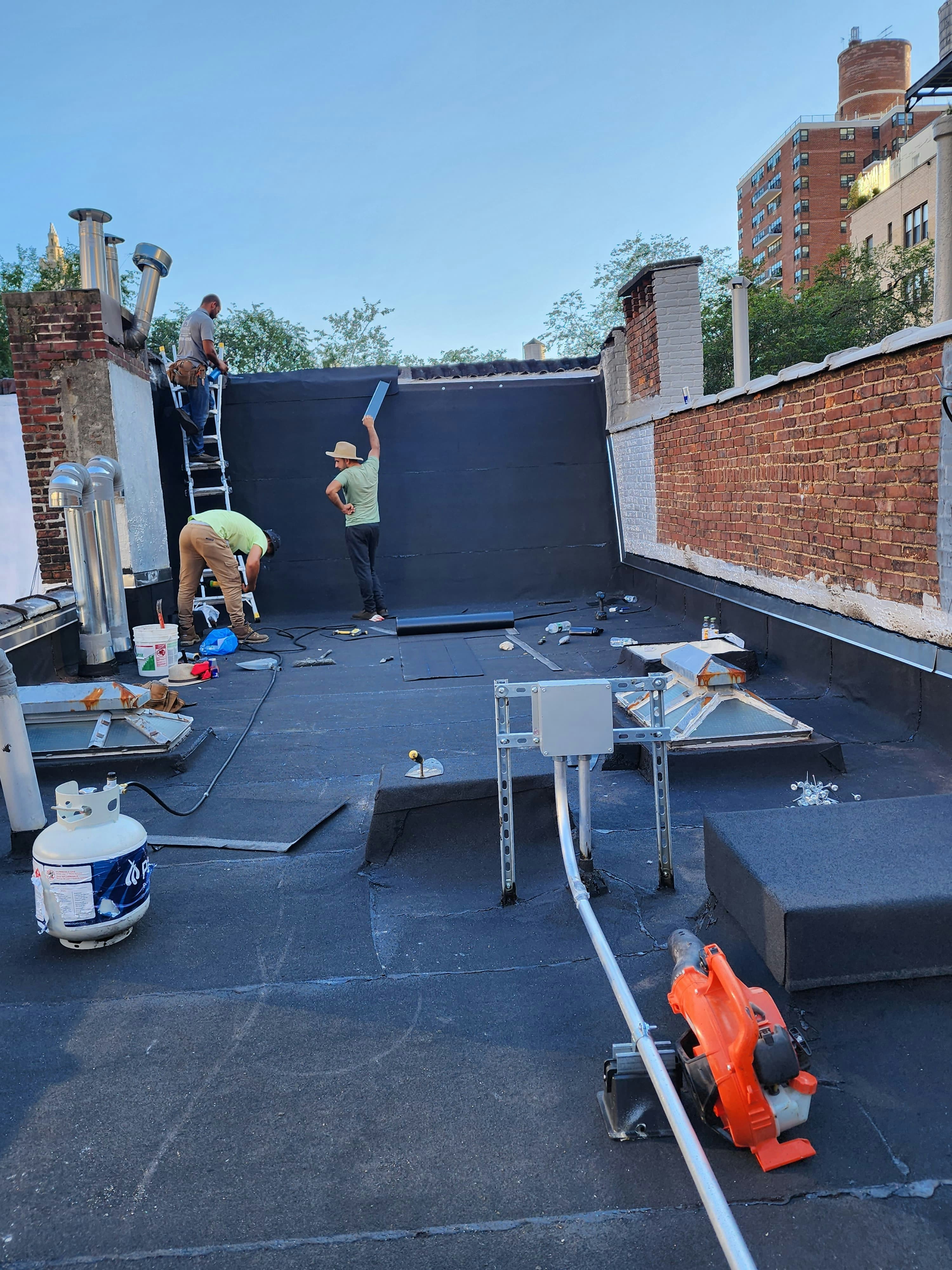 Commercial flat roofing installation on large industrial building, workers visible, bright sky