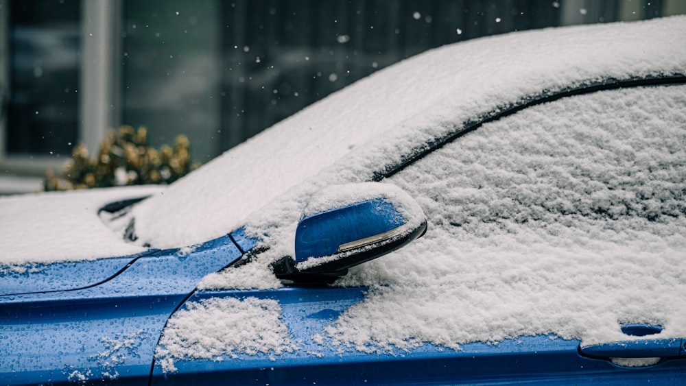 a blue car covered in snow in front of a building