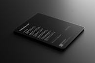 A sleek, black tablet-like object rests on a dark surface, displaying illuminated text in a minimalist style. The text includes features and information about a mock-up, primarily in white font, conveying a modern and professional look.