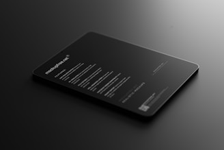 A sleek, black tablet-like object rests on a dark surface, displaying illuminated text in a minimalist style. The text includes features and information about a mock-up, primarily in white font, conveying a modern and professional look.