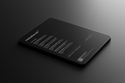 A sleek, black tablet-like object rests on a dark surface, displaying illuminated text in a minimalist style. The text includes features and information about a mock-up, primarily in white font, conveying a modern and professional look.