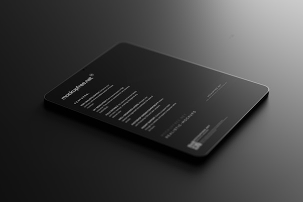 A sleek, black tablet-like object rests on a dark surface, displaying illuminated text in a minimalist style. The text includes features and information about a mock-up, primarily in white font, conveying a modern and professional look.