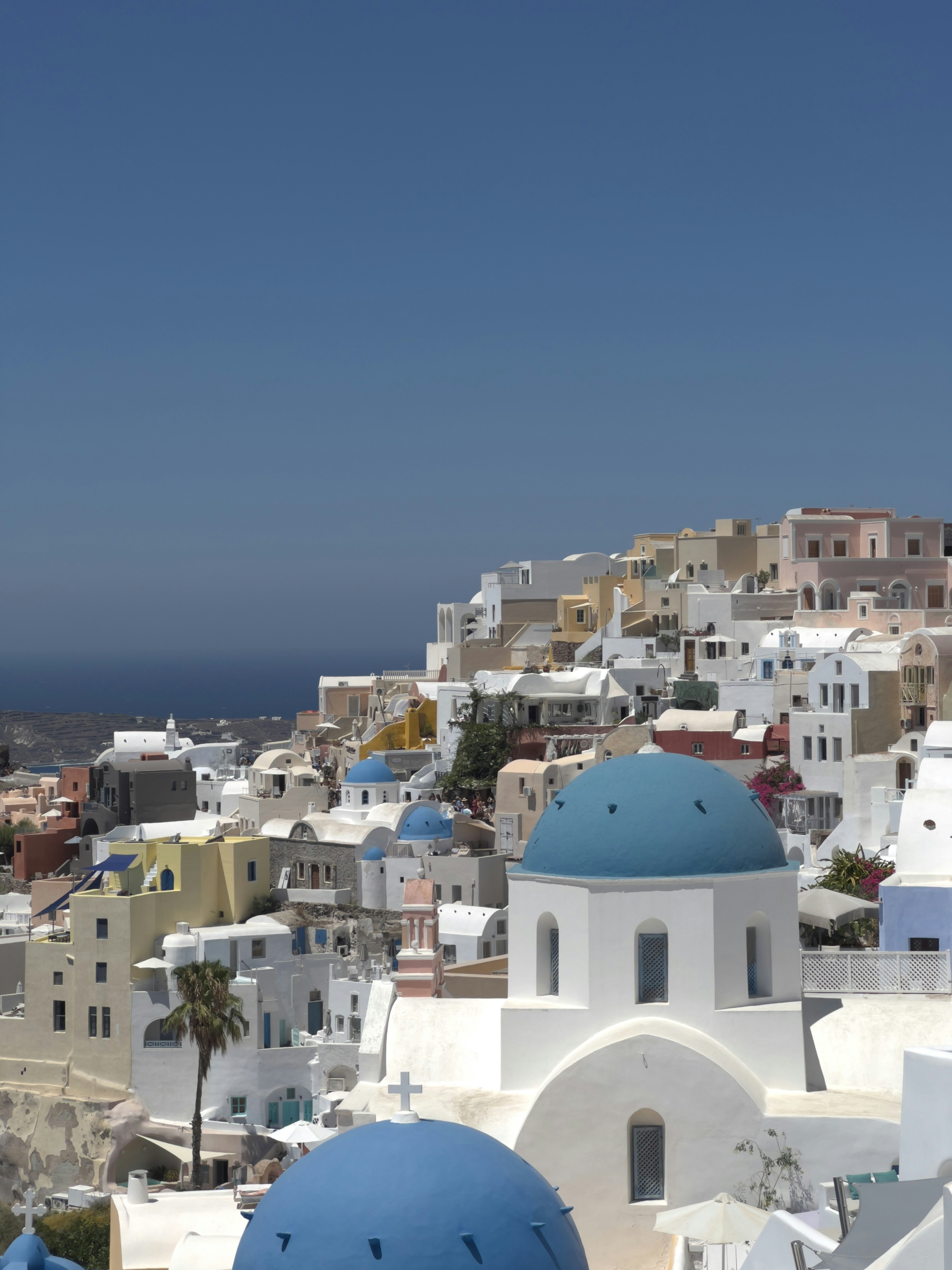Bright white Santorini buildings with blue domes, well-lit Mediterranean scene, open sky above the caldera
