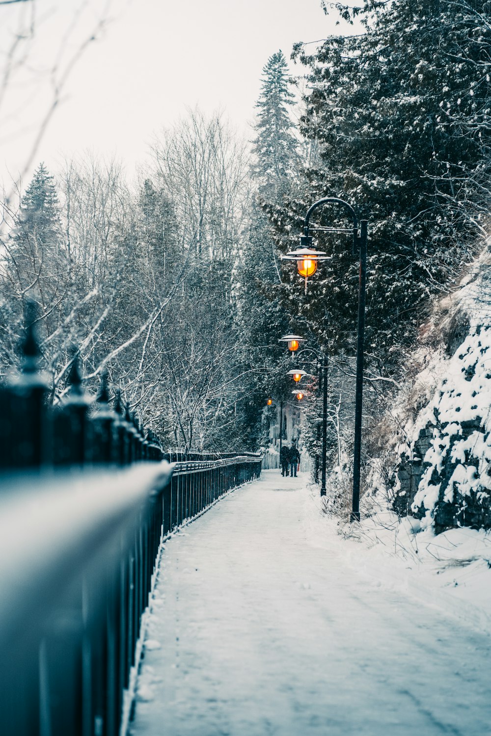 a street light on a snowy street next to a fence