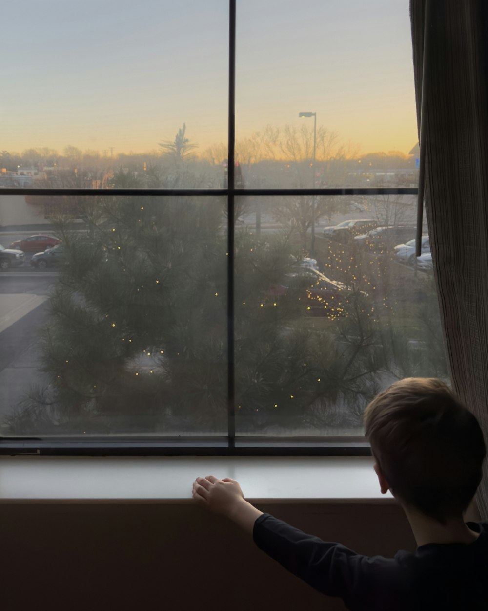 a young boy looking out a window at a parking lot