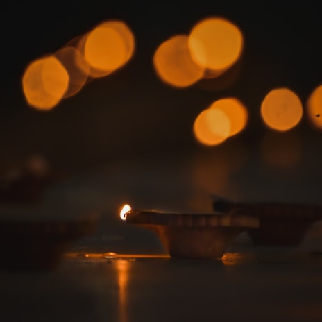 An orange-hued image of a diya lamp glowing softly against a backdrop of marigold flowers.