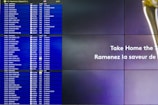 A split-screen image shows a digital airport departure board on the left with flight information for various U.S. destinations and an advertisement on the right side. The flight board displays destination, flight number, gate, and status for flights in French and English. The advertisement features text that likely promotes a product or service.