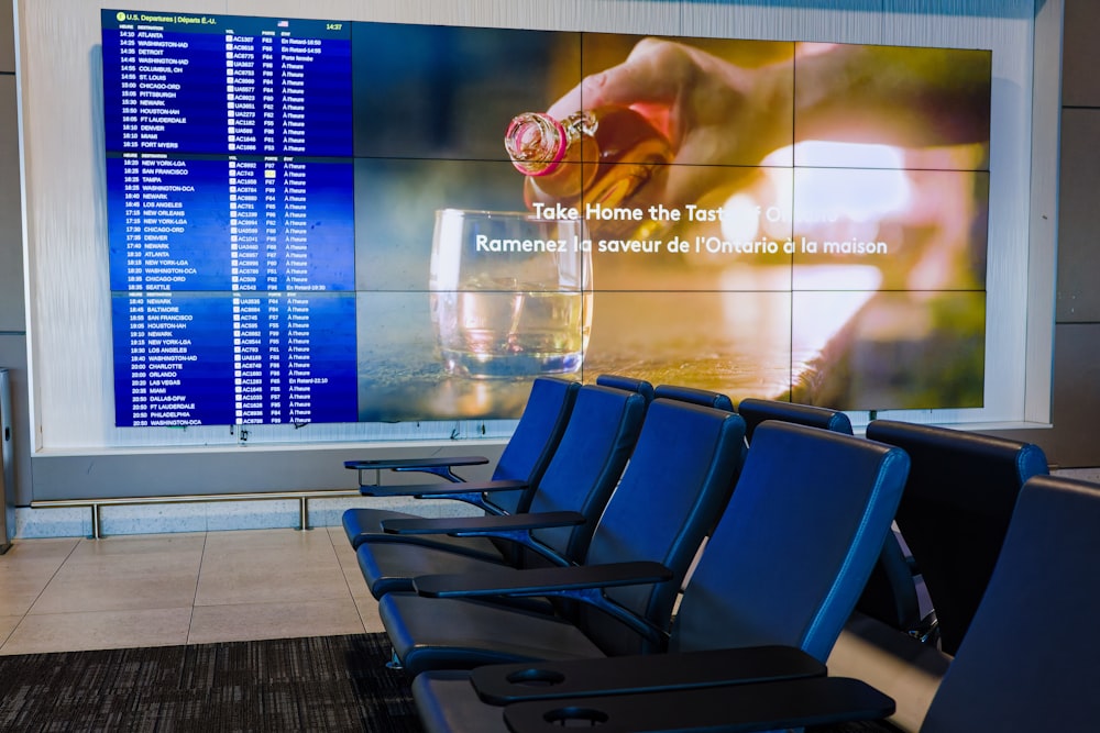 a row of blue chairs sitting in front of a large screen