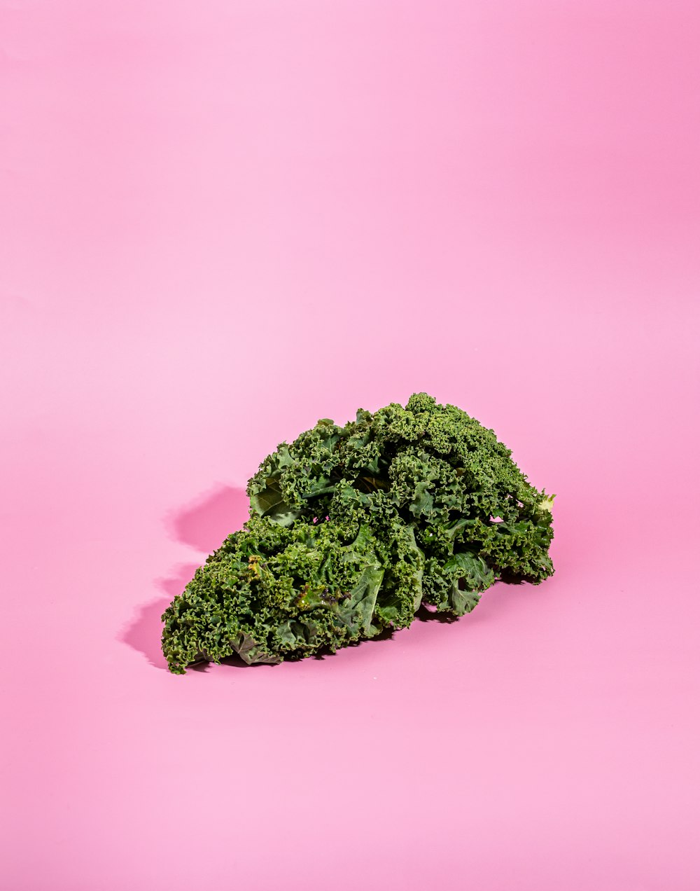 a pile of green leafy vegetables on a pink background