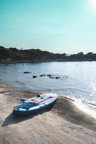 Close-up of a paddle board resting on the shore with morning sunlight reflecting on the water.