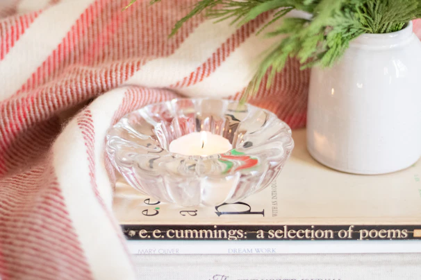 A cozy corner featuring a colorful ceramic pitcher beside a stack of books and a warm candle.